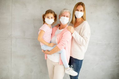 Son sınıf öğrencisi, yetişkin bir kadın ve sevimli küçük bir kız. Üç nesildir evde koruyucu yüz maskeleri takıyor.