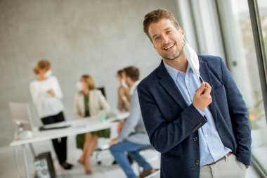 Yakışıklı genç iş adamı ofis alanında koruyucu maskesini çıkarıyor.