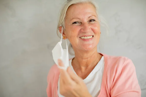 Portrait of senior woman taking off protective medical facial mask for protection from virus