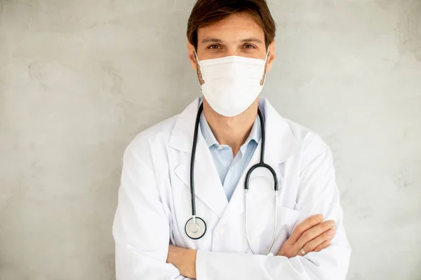 Atrakcyjny Młody Lekarz Noszący Chirurgiczną Maskę Ochronną Stojący Przy Ścianie — Zdjęcie stockowe
