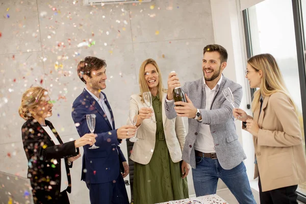 Group of excited business people celebrating and toasting with confetti falling in the office