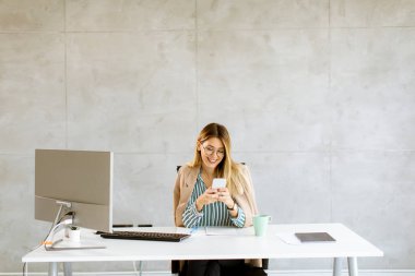 Ofisteki masada otururken cep telefonu kullanan genç ve güzel bir kadın.