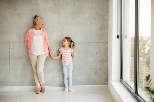 Liten Flicka Med Sin Mormor Stående Vid Den Grå Väggen — Stockfoto