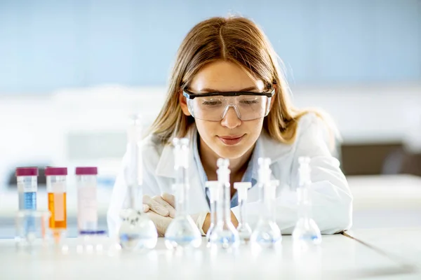 研究室での解決策を備えたフラスコを見ている若い女性医学または科学研究者 — ストック写真