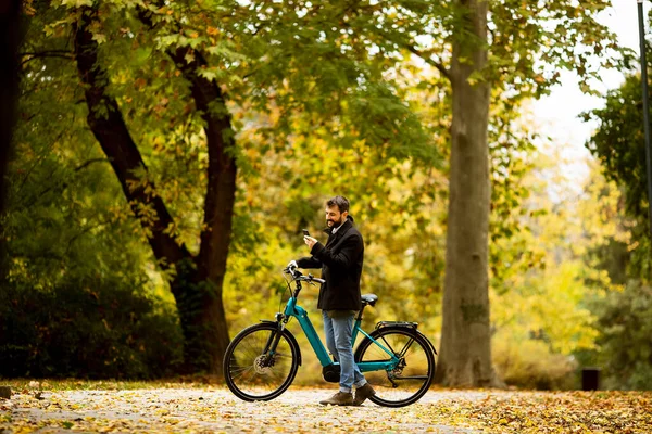 Joven Guapo Con Bicicleta Eléctrica Usando Teléfono Móvil Parque Otoño — Foto de Stock