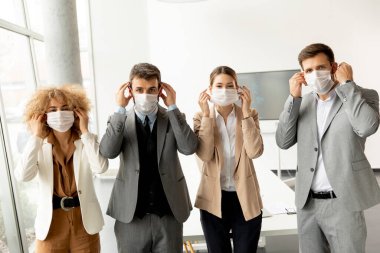 İş adamları koruyucu maskelerini çıkarıp ofisteki kameraya bakıyor.