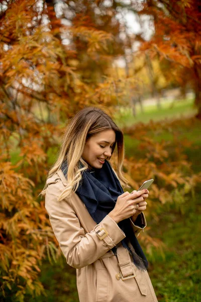 美丽的年轻女子在秋天的公园里用手机 — 图库照片