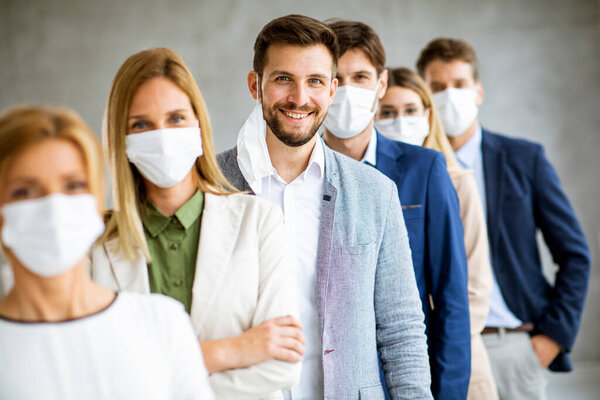 Business man taking off hisprotective facial mask and looking at the camera with histeam members standing in the line at the office