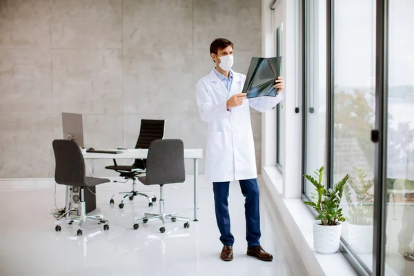 Médico Joven Con Máscara Facial Protectora Examinando Rayos Consultorio — Foto de Stock