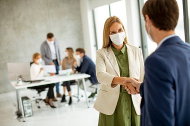 Birkaç iş adamı ofiste el sıkışıyor ve koronavirüs salgınından dolayı koruyucu maskeler takıyor.