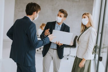 Ofiste dizüstü bilgisayarı olan iki genç adam ve kadın arkalarında genç insanlarla birlikte çalışıyor.