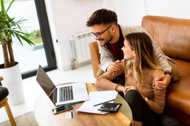 Yakışıklı genç çift evdeki kanepede otururken birlikte dizüstü bilgisayar kullanıyorlar.