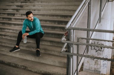 Genç adam eğitim sırasında şehir ortamında bir şişe suyla dinleniyor.