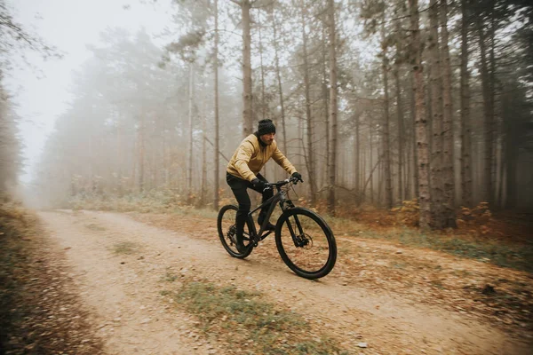 Handsome young man biking through autumn forest