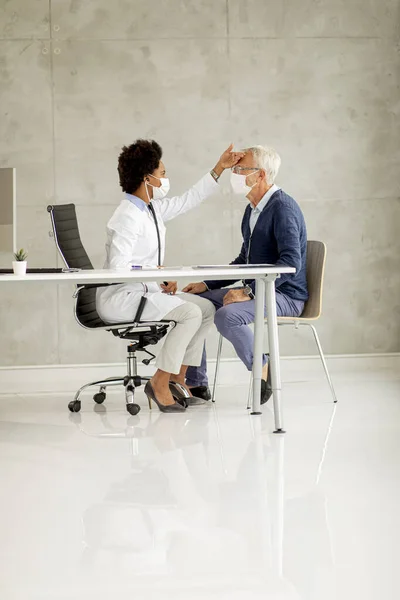 Senior man with protective facial mask receive news from black female doctor in the office