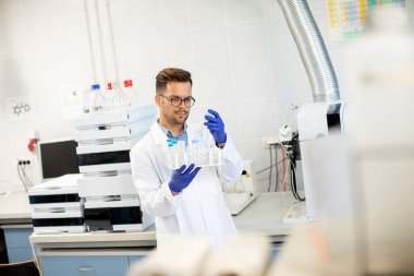 Laboratuvarda HPLC sistemi ve kromatografi ekipmanları ile kimyasal örnekler üzerinde çalışan yakışıklı genç bir araştırmacı