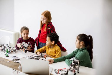 Robot sınıfında elektrikli oyuncak ve robot programlayan bir grup mutlu çocuk.
