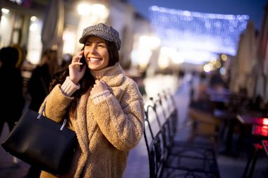 Noel zamanı sokakta cep telefonunu kullanan güzel genç bir kadın.