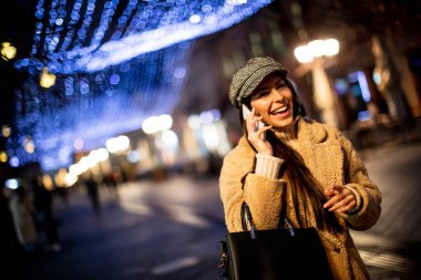 Noel zamanı sokakta cep telefonunu kullanan güzel genç bir kadın.