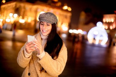 Noel zamanı sokakta cep telefonunu kullanan güzel genç bir kadın.