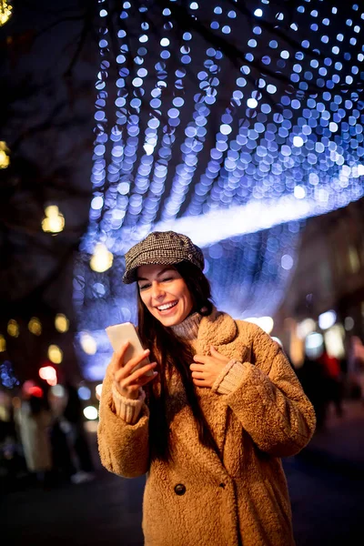 Beautiful young woman using her mobile phone in the street at Christmas time