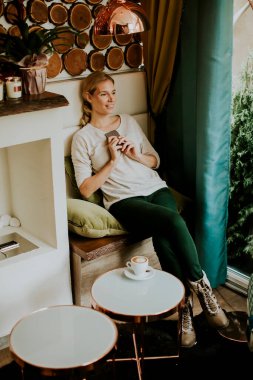 Kahve ya da cappuccino ile bir masada oturan ve cep telefonu kullanan güzel genç bir kadın.