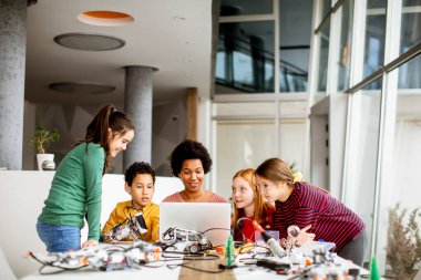 Bir grup mutlu çocuk ve dizüstü bilgisayarı olan Afrika kökenli Amerikalı kadın fen öğretmenleri robot sınıfında elektrikli oyuncaklar ve robotlar programlıyorlar.