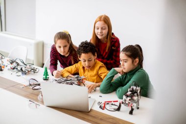 Robot sınıfında elektrikli oyuncak ve robot programlayan bir grup mutlu çocuk.