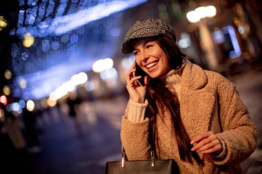 Noel zamanı sokakta cep telefonunu kullanan güzel genç bir kadın.