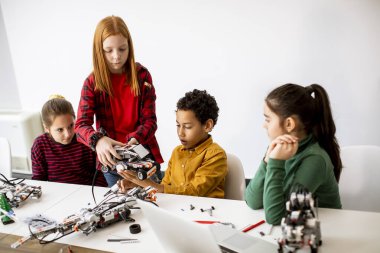 Robot sınıfında elektrikli oyuncak ve robot programlayan bir grup mutlu çocuk.