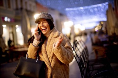 Noel zamanı sokakta cep telefonunu kullanan güzel genç bir kadın.