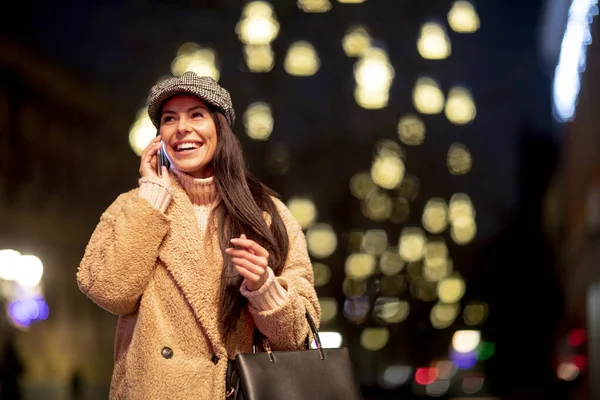Noel zamanı sokakta cep telefonunu kullanan güzel genç bir kadın.