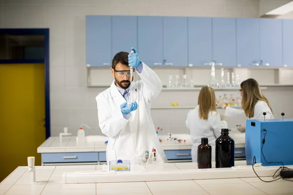 实验室里站着一位年轻英俊的保护工作服研究人员 用液体分析瓶子 — 图库照片