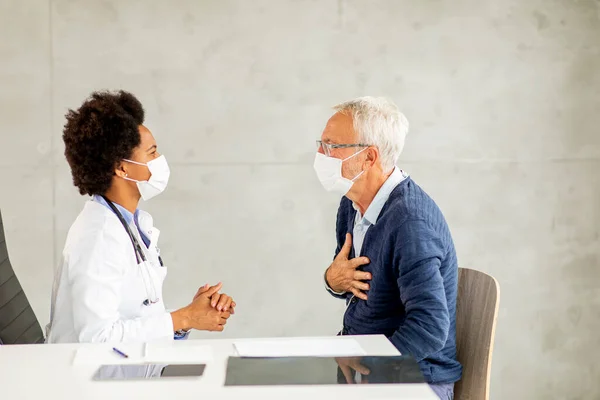 Senior man with protective facial mask receive news from black female doctor in the office