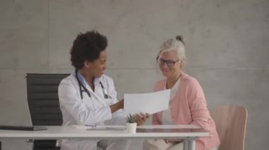 Koruyucu maske takan yaşlı bir kadın ofiste siyahi bir kadın tarafından muayene ediliyor.