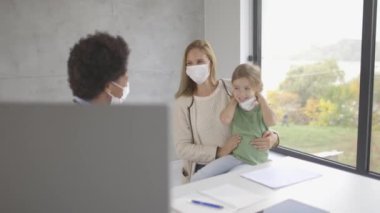 Anne ve küçük kızı Afrikalı Amerikalı kadın doktor tarafından pediatri muayenesinde.