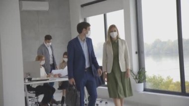 Ofiste Corona virüsünü önlemek için koruyucu maskeler takan yakışıklı genç iş çifti.