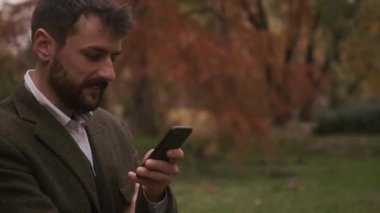 Güz parkında cep telefonu kullanan yakışıklı genç adam.