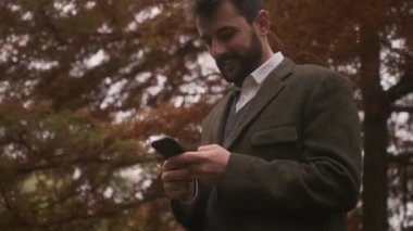 Güz parkında cep telefonu kullanan yakışıklı genç adam.