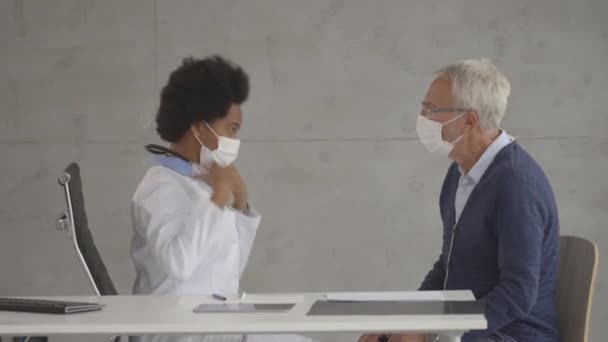안면 마스크를 쓰고 있는 노인 이 사무실에 있는 흑인 여성 의사로부터 소식을 받는다 — 비디오