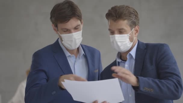 Zwei Hübsche Junge Geschäftsleute Mit Gesichtsschutzmasken Diskutieren Büro Mit Papierplan — Stockvideo