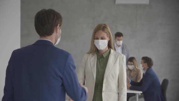 事務所で握手をしたり コロナウイルスの流行による保護面を身に着けているビジネスマンのカップル — ストック動画