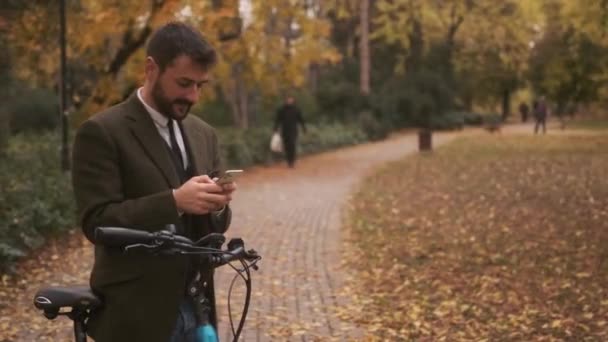Schöner junger Mann mit Elektrofahrrad und Handy im Herbstpark