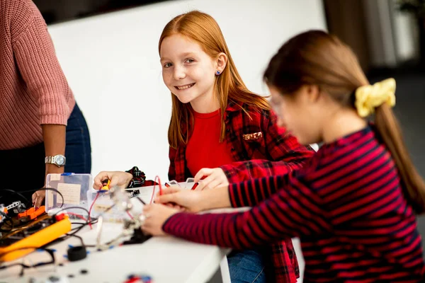Group of cute little girls programming electric toys and robots at robotics classroom