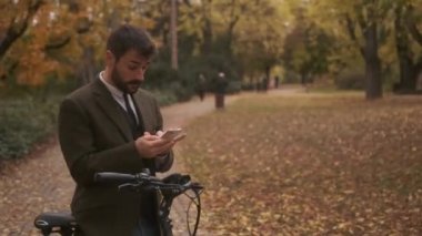 Sonbahar parkında cep telefonu kullanan elektrikli bisikletli yakışıklı bir genç.