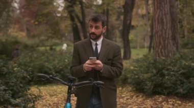 Sonbahar parkında cep telefonu kullanan elektrikli bisikletli yakışıklı bir genç.