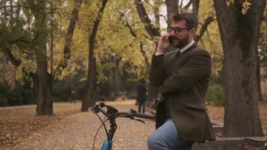 Sonbahar parkında cep telefonu kullanan elektrikli bisikletli yakışıklı bir genç.