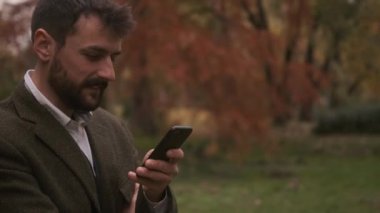 Güz parkında cep telefonu kullanan yakışıklı genç adam.