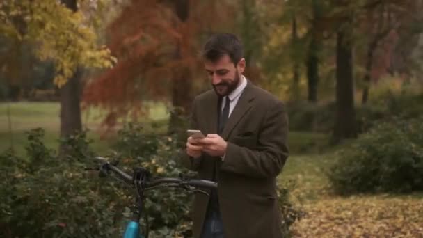 Bonito Jovem Com Bicicleta Elétrica Usando Telefone Celular Parque Outono — Vídeo de Stock