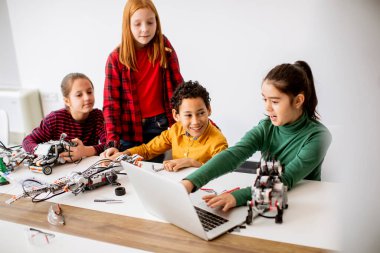 Robot sınıfında elektrikli oyuncak ve robot programlayan bir grup mutlu çocuk.